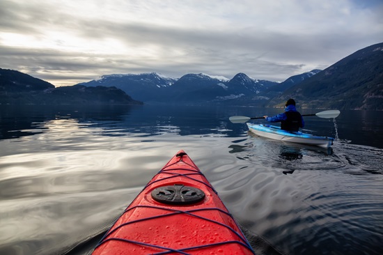 21 things to do in norwayAdventurous man kayaking in peaceful water during a cloudy winter day.